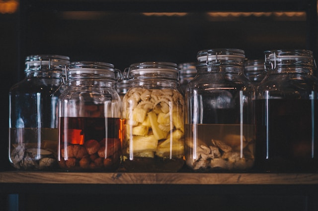 Jars of pickled foods on a wooden shelf, representing food preservation.