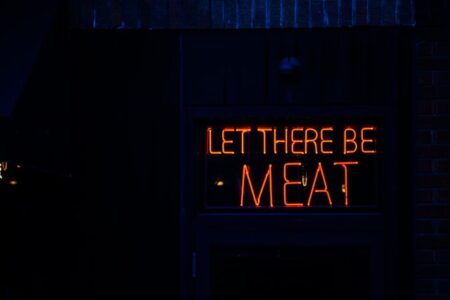 Neon sign reading "LET THERE BE MEAT" on a dark building.