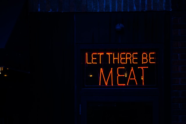 Neon sign reading "LET THERE BE MEAT" on a dark building.