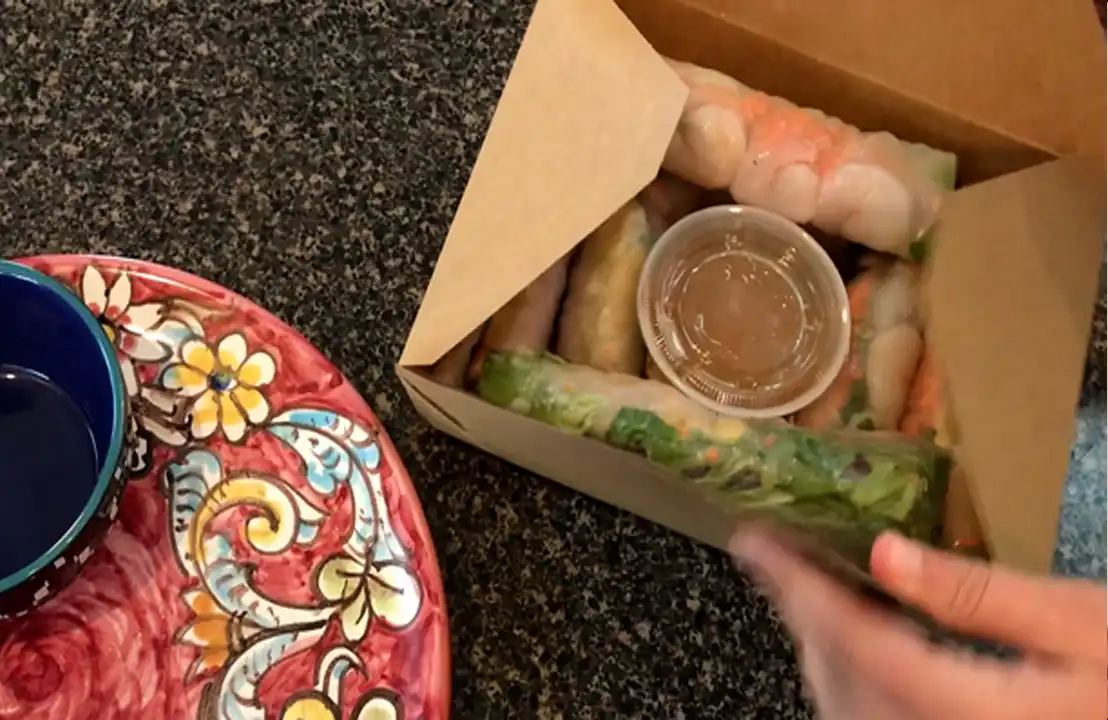 Spring rolls takeout with dipping sauce on countertop.