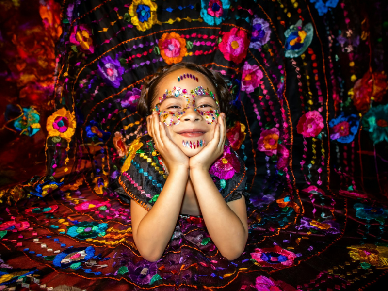 Girl with face paint smiles against a vibrant, colorful embroidered textile backdrop.