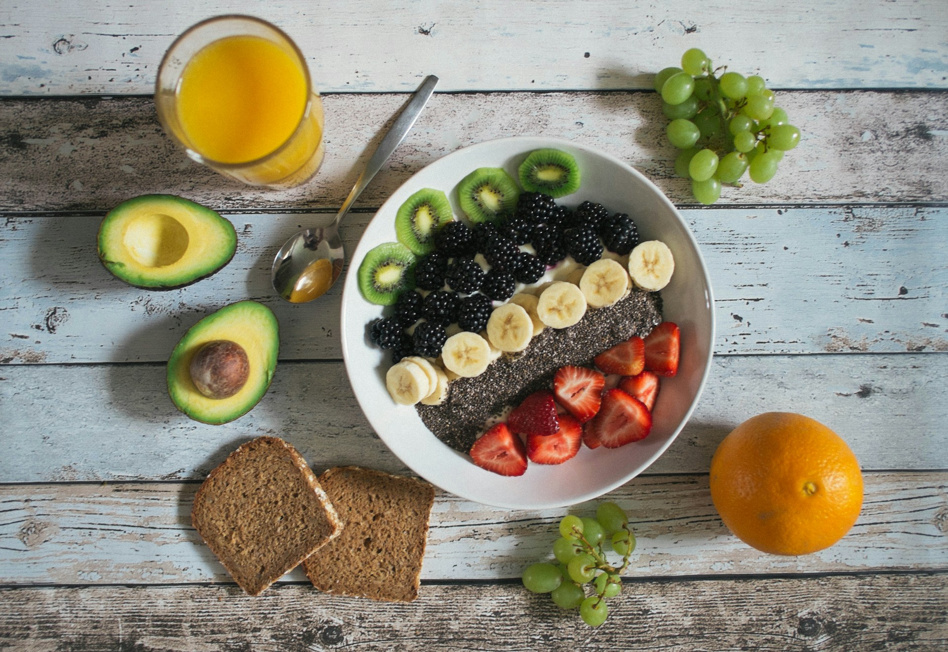 Healthy breakfast bowl with fruit, chia seeds, and avocado, alongside whole wheat toast and orange juice.