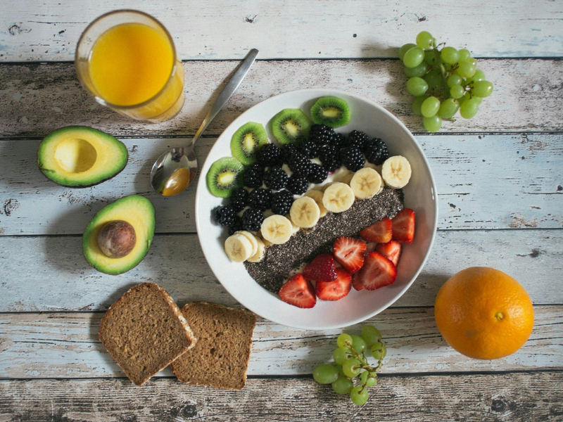 Healthy breakfast bowl with fruit, avocado, juice, and whole wheat bread on a wooden table.
