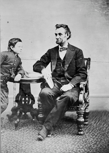 Abraham Lincoln sits in a chair next to a boy at a small table.