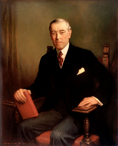 Formal portrait of President Woodrow Wilson seated, holding a red book.