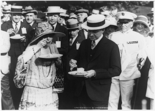 Calvin Coolidge and guests in hats enjoy a meal outdoors