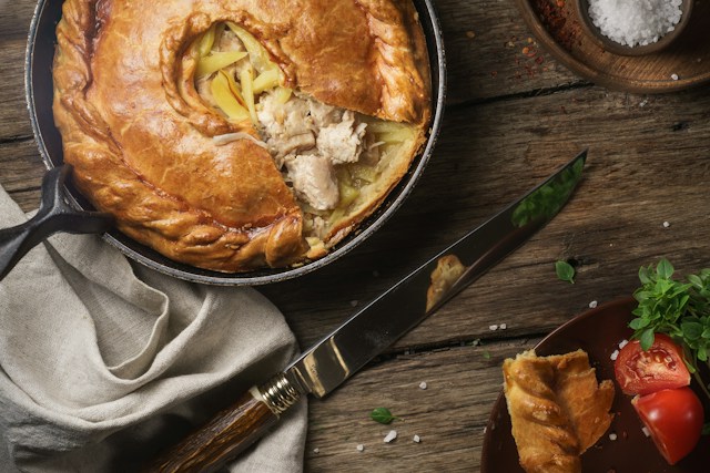 Golden-brown chicken pot pie with flaky crust, served with tomatoes and herbs.