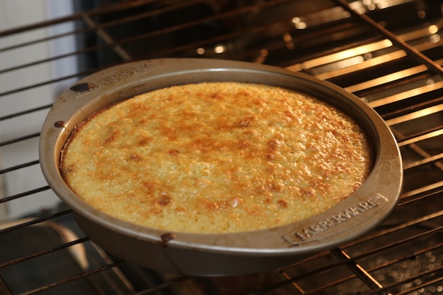 Golden-brown cornbread baking in a round pan inside an oven.
