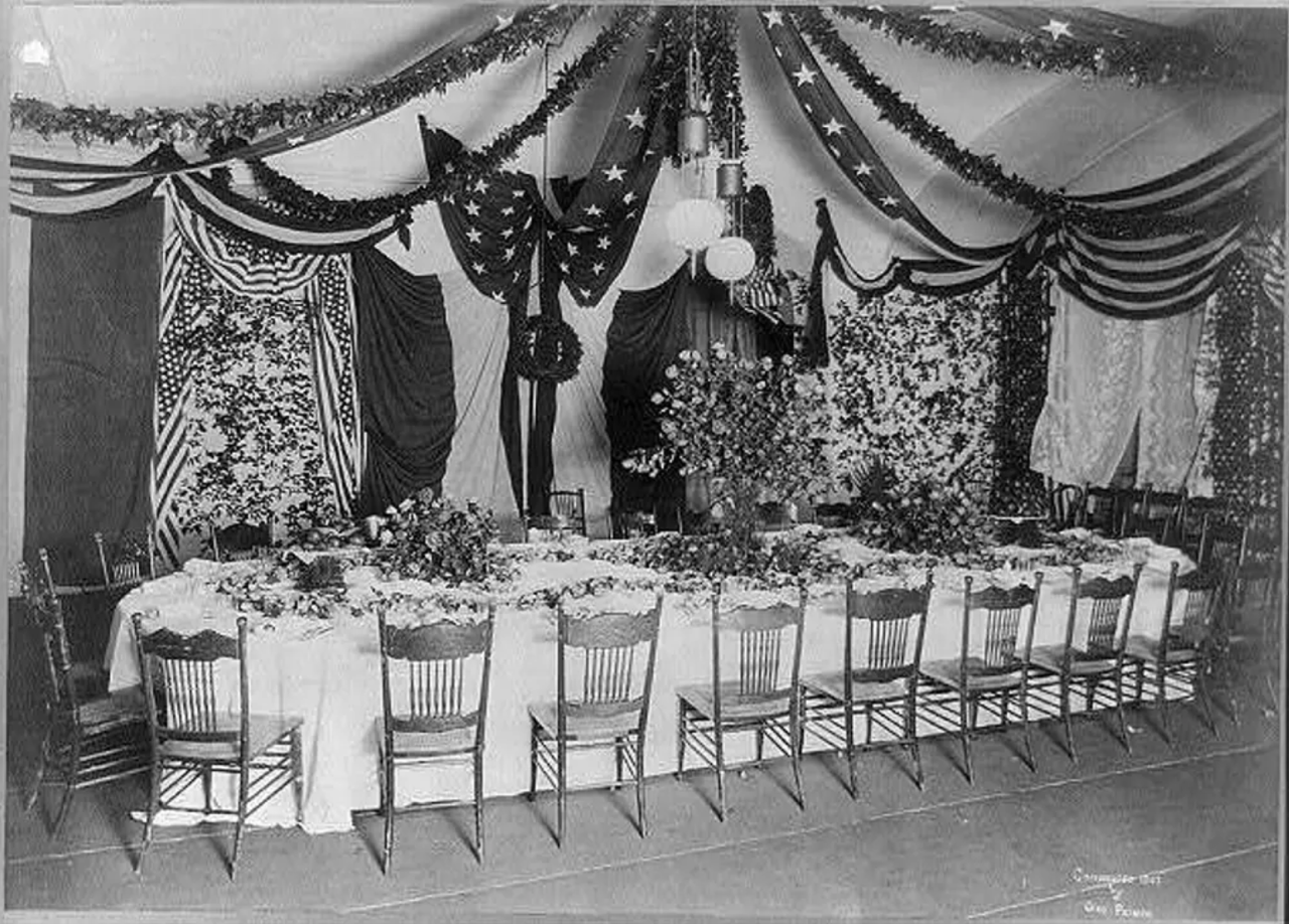 William McKinley seated at a long banquet table decorated with flags and flowers