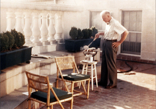 Dwight D. Eisenhower grilling outdoors on a patio with chairs.