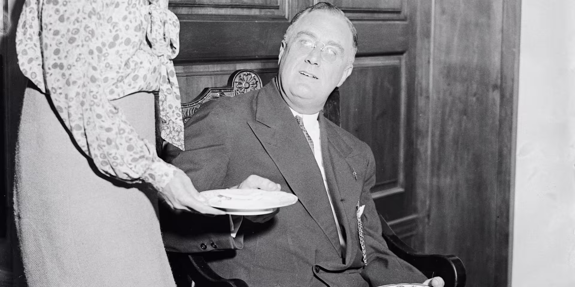 Franklin D. Roosevelt seated, being served by a woman