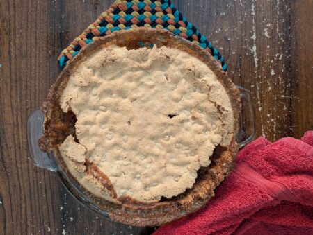Overbaked pie in a glass dish with colorful potholders