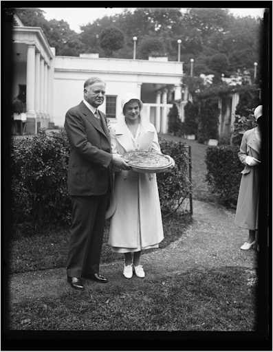 Herbert Hoover and Lou Henry Hoover present a pie outdoors.