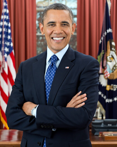 Barack Obama smiling and posing with arms crossed in the Oval Office