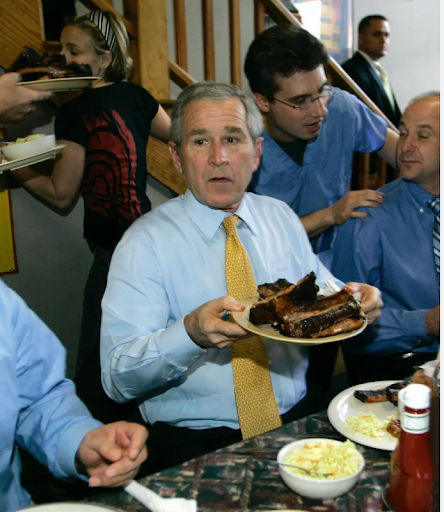 George W. Bush holds a plate of ribs at a meal with others.