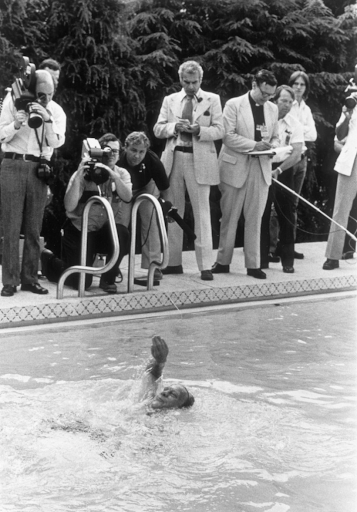 Gerald Ford swims in a pool as reporters and onlookers watch.